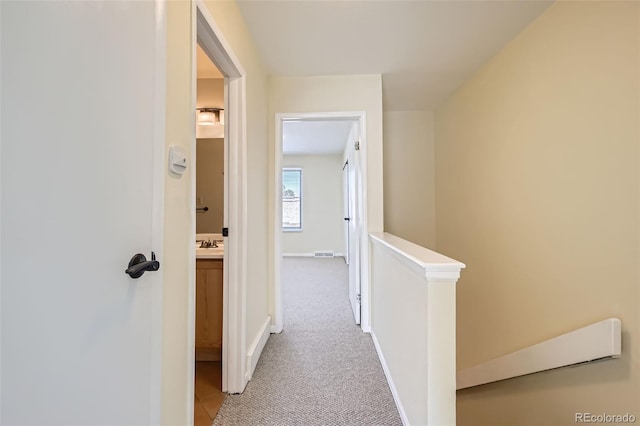 hall featuring light carpet, baseboards, a sink, and an upstairs landing