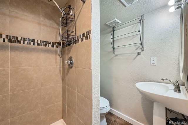 full bath with toilet, tiled shower, and wood finished floors