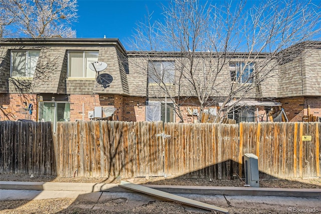 exterior space with a shingled roof, brick siding, a fenced front yard, and mansard roof