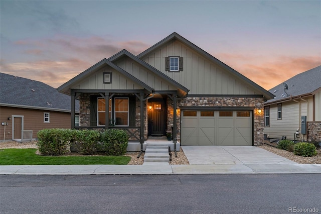 craftsman-style home featuring covered porch, a garage, concrete driveway, stone siding, and board and batten siding