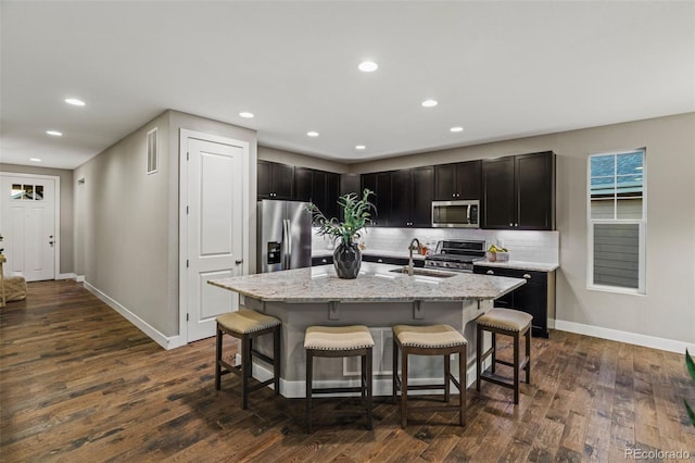 kitchen with stainless steel appliances, a sink, a kitchen bar, and dark wood-style floors