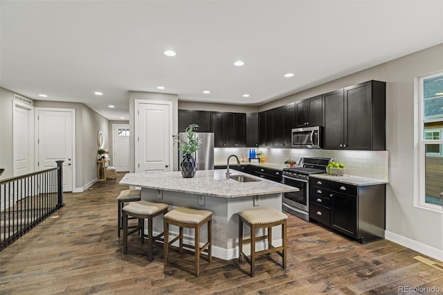 kitchen with a breakfast bar, stainless steel appliances, tasteful backsplash, a sink, and dark cabinets