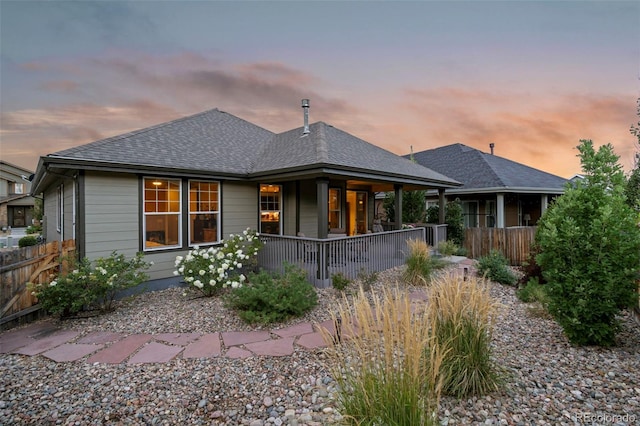 rear view of house with a porch, fence, and a shingled roof