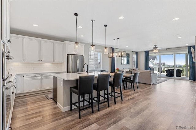 7074 S Vandriver Ct, Aurora, CO 80016 - kitchen with stainless steel refrigerator, open floor plan, decorative backsplash, white cabinets, and wood finished floors