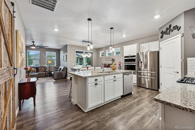 kitchen with a barn door, stainless steel appliances, white cabinetry, and a center island with sink