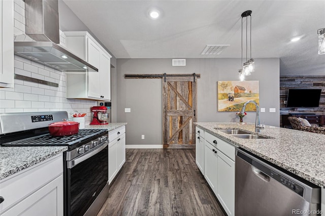 kitchen featuring white cabinets, wall chimney range hood, sink, a barn door, and appliances with stainless steel finishes