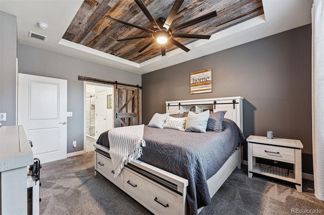 carpeted bedroom with connected bathroom, a barn door, ceiling fan, and a tray ceiling