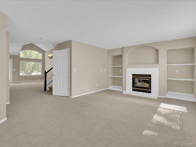 8906 Miners Dr, Highlands Ranch, CO 80126 - unfurnished living room with carpet, built in shelves, a glass covered fireplace, lofted ceiling, and stairs