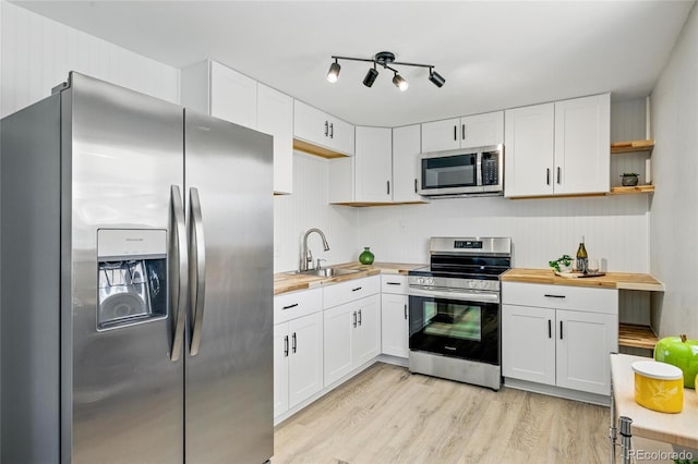 kitchen featuring appliances with stainless steel finishes, wood counters, a sink, white cabinetry, and light wood-style flooring