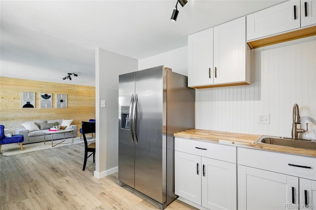 kitchen featuring stainless steel fridge with ice dispenser, wood walls, a sink, rail lighting, and light wood-type flooring