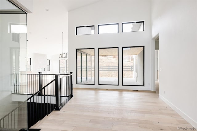 hall with light hardwood / wood-style floors and a towering ceiling