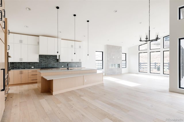 kitchen with backsplash, pendant lighting, light hardwood / wood-style floors, white cabinetry, and an island with sink