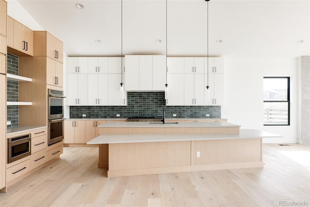 kitchen featuring appliances with stainless steel finishes, pendant lighting, a center island with sink, light hardwood / wood-style flooring, and white cabinetry