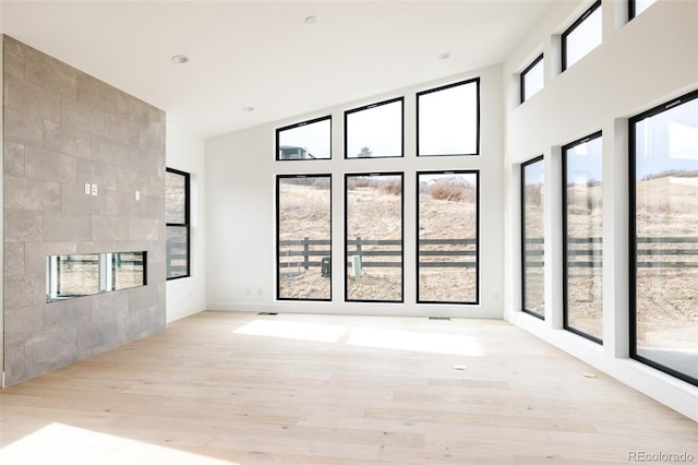 spare room with light hardwood / wood-style floors, a towering ceiling, and a tiled fireplace