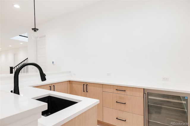 kitchen featuring decorative light fixtures, light brown cabinetry, sink, and beverage cooler