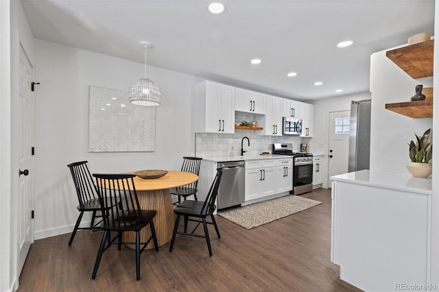 kitchen featuring pendant lighting, backsplash, white cabinets, dark hardwood / wood-style flooring, and stainless steel appliances