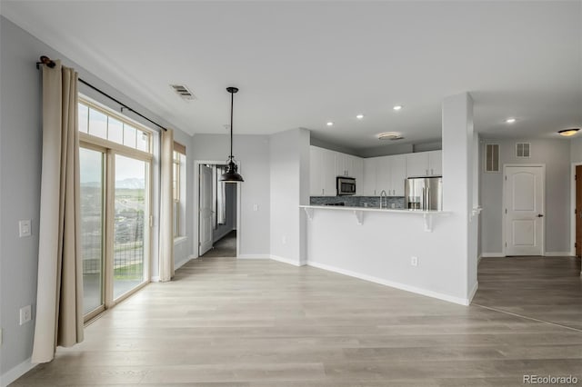 13456 Via Varra Unit 401, Broomfield, CO 80020 - kitchen with appliances with stainless steel finishes, a kitchen breakfast bar, white cabinetry, recessed lighting, and light wood finished floors