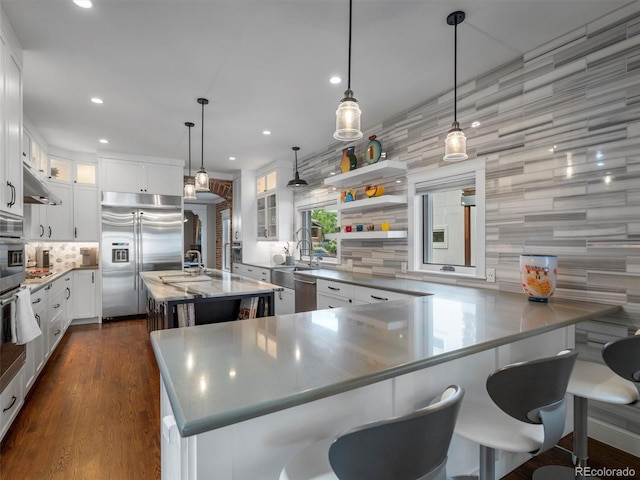 kitchen featuring white cabinets, appliances with stainless steel finishes, backsplash, hanging light fixtures, and a center island with sink