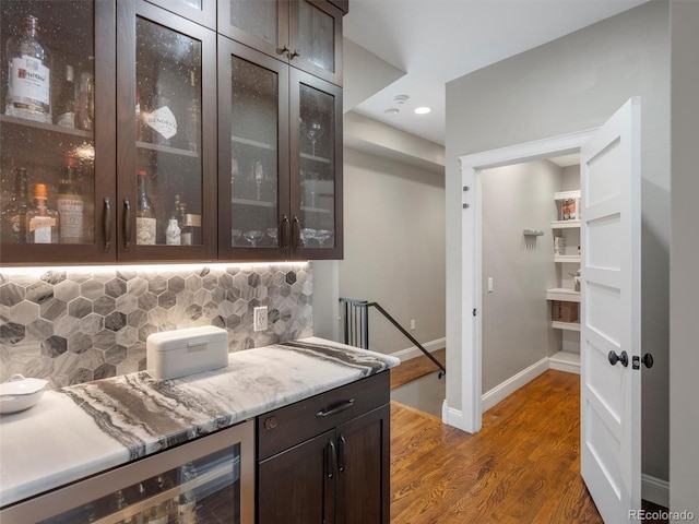 bar with backsplash, wine cooler, light stone countertops, and dark brown cabinetry