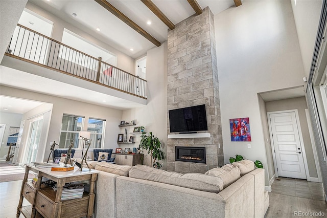 living room with beamed ceiling, a tile fireplace, light hardwood / wood-style flooring, and high vaulted ceiling