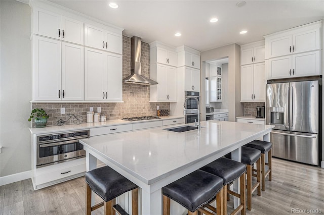 kitchen with wall chimney range hood, a breakfast bar area, an island with sink, and stainless steel appliances