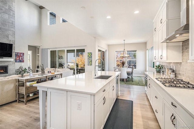 kitchen with a fireplace, a kitchen island with sink, light hardwood / wood-style flooring, wall chimney range hood, and pendant lighting