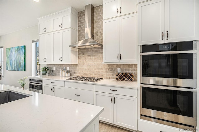 kitchen with stainless steel appliances, sink, wall chimney exhaust hood, backsplash, and white cabinets