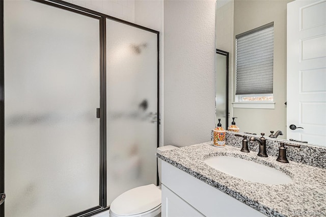 bathroom featuring toilet, vanity, and a shower with shower door