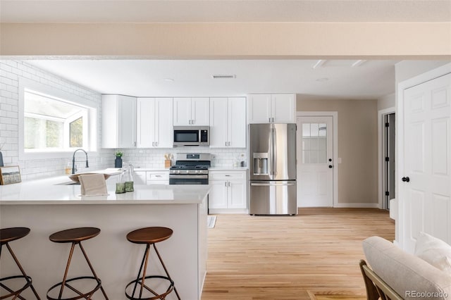 kitchen featuring a breakfast bar area, stainless steel appliances, white cabinets, decorative backsplash, and light hardwood / wood-style flooring