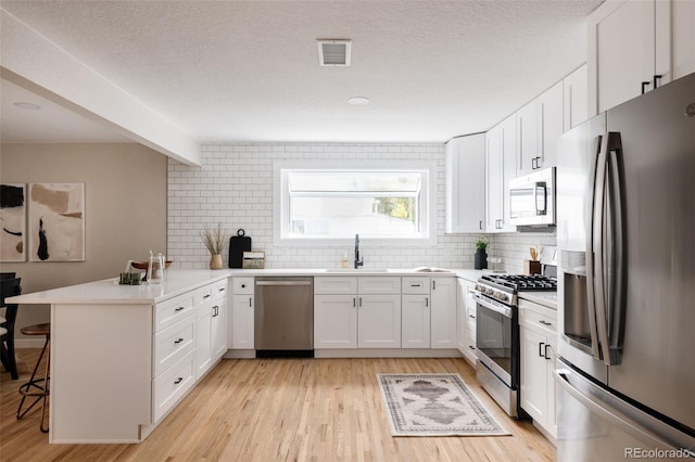 kitchen featuring sink, light wood-type flooring, a kitchen bar, kitchen peninsula, and stainless steel appliances