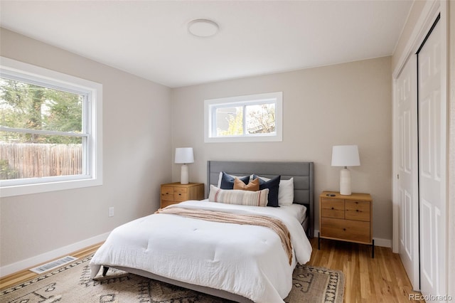 bedroom with a closet, light hardwood / wood-style flooring, and multiple windows