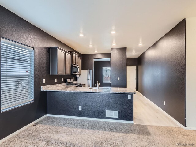 kitchen with kitchen peninsula, stainless steel appliances, and light stone countertops