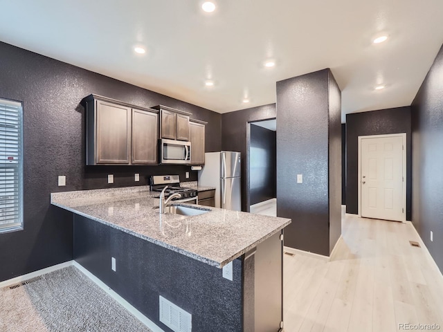 kitchen with sink, light hardwood / wood-style flooring, light stone countertops, appliances with stainless steel finishes, and kitchen peninsula