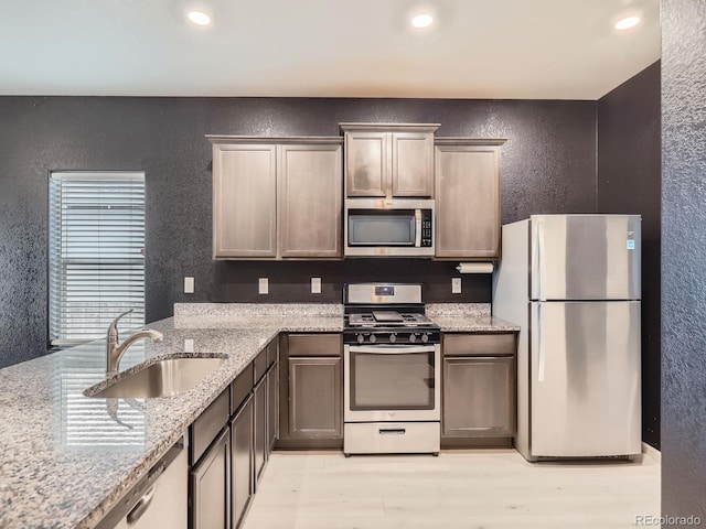 kitchen featuring light wood-type flooring, light stone countertops, sink, and appliances with stainless steel finishes