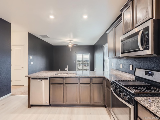 kitchen with sink, light stone countertops, dark brown cabinets, kitchen peninsula, and stainless steel appliances