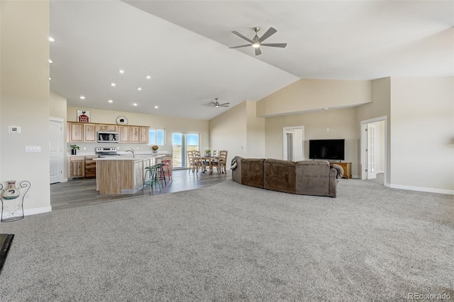 unfurnished living room with light carpet, ceiling fan, sink, and high vaulted ceiling