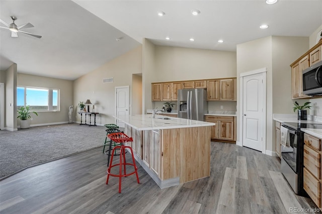 kitchen featuring appliances with stainless steel finishes, light hardwood / wood-style floors, a kitchen bar, ceiling fan, and a kitchen island with sink