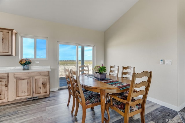 dining room featuring light wood-type flooring, baseboards, vaulted ceiling, and visible vents