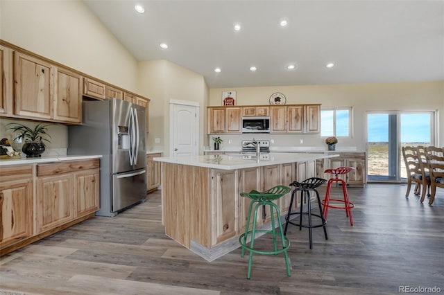 kitchen with light hardwood / wood-style floors, an island with sink, vaulted ceiling, a kitchen bar, and stainless steel appliances