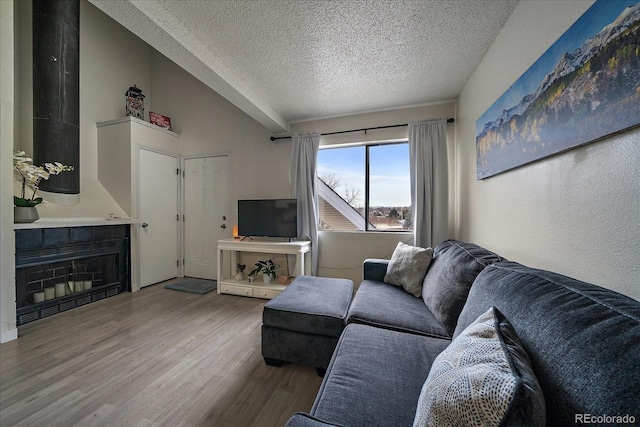 living room featuring a tiled fireplace, vaulted ceiling, a textured ceiling, and wood finished floors