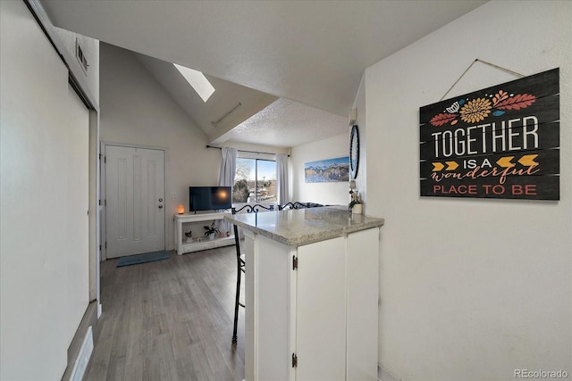 kitchen with lofted ceiling with skylight, a breakfast bar, wood finished floors, white cabinets, and a textured ceiling