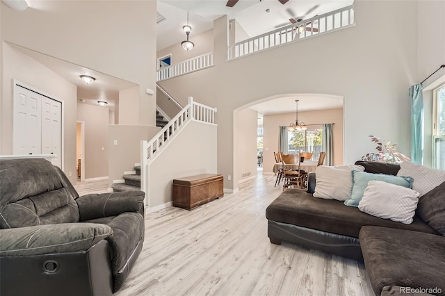 living area with arched walkways, ceiling fan with notable chandelier, a high ceiling, stairway, and light wood-type flooring