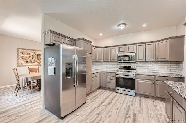 kitchen with light wood finished floors, appliances with stainless steel finishes, gray cabinets, and backsplash