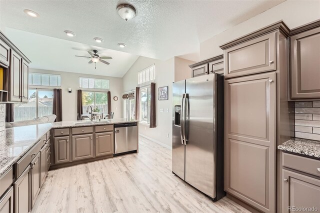 kitchen featuring stainless steel appliances, decorative backsplash, vaulted ceiling, a sink, and light stone countertops