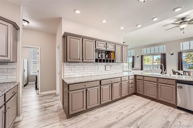 kitchen featuring light stone counters, a sink, light wood-type flooring, dishwasher, and tasteful backsplash