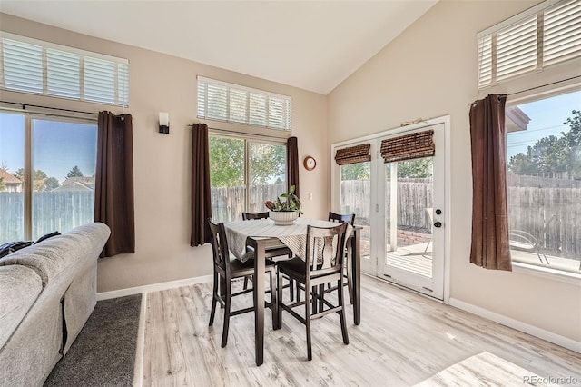 dining space featuring light wood-style floors, high vaulted ceiling, and baseboards