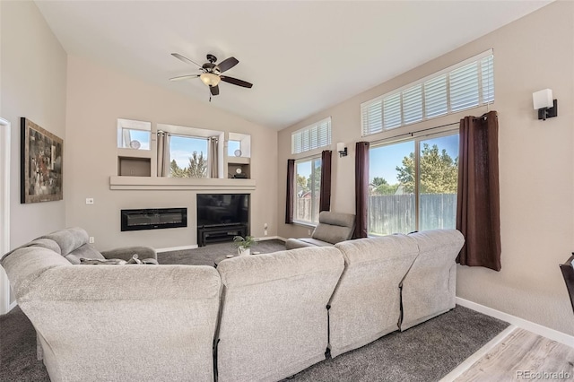 living area with baseboards, a ceiling fan, a glass covered fireplace, wood finished floors, and vaulted ceiling