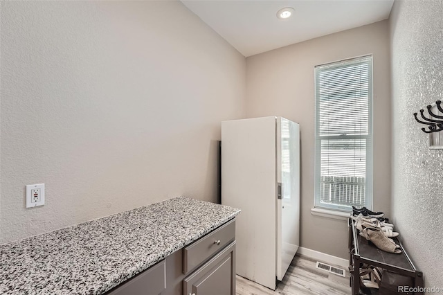 kitchen with light wood finished floors, baseboards, visible vents, a textured wall, and light stone counters