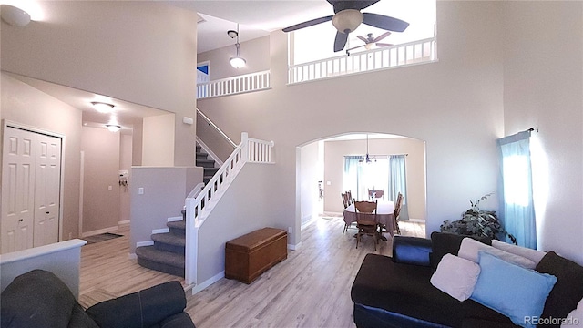 living area featuring arched walkways, light wood-style flooring, a towering ceiling, a ceiling fan, and stairs