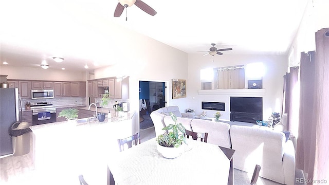 dining room with ceiling fan, vaulted ceiling, and a glass covered fireplace